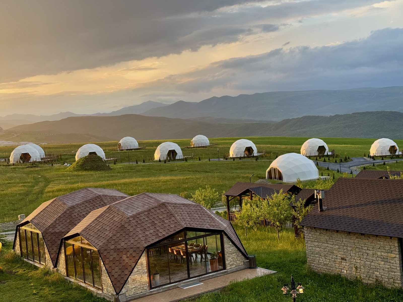 GlampingHouse dome resort on a mountain plateau at sunset, shingled restaurant domes in the foreground