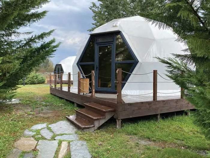 White geodesic dome with glazed front and wooden deck in a forest clearing
